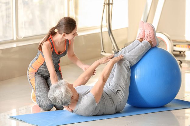 young-trainer-heYoung trainer helping elderly woman during training in gymlping-elderly-woman-during-training-in-gym Young trainer helping elderly woman during training in gym