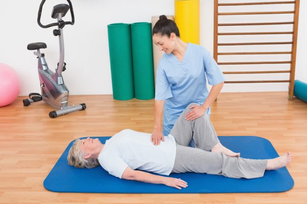 Therapist working with senior woman on exercise mat in fitness studio Therapist working with senior woman on exercise mat in fitness studio