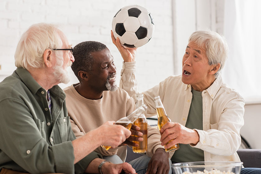 Asian man holding football near multiethnic friends with beer at home Asian man holding football near multiethnic friends with beer at home