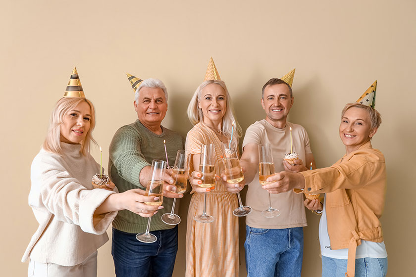 Mature people with tartlets and champagne celebrating Birthday on beige background