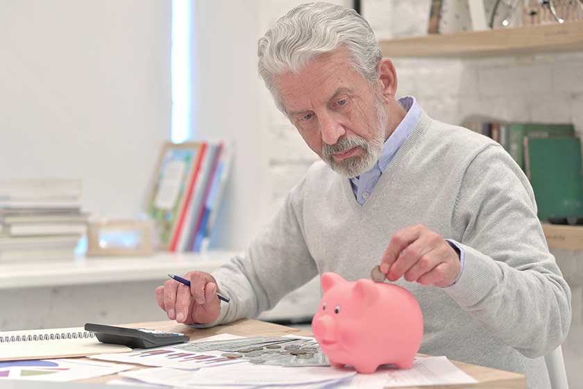 Senior Old Man Putting Coin in Piggy Bank