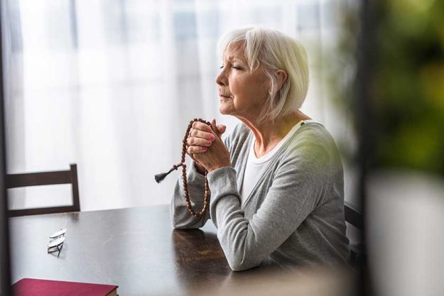 Senior woman holding wooden rosary and praying with closed eyes Senior woman holding wooden rosary and praying with closed eyes