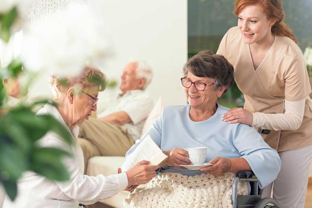 Two senior pensioners enjoying their leisure time together inside a private nursing home. Tender caretaker in uniform standing next to them Two senior pensioners enjoying their leisure time together inside a private nursing home. Tender caretaker in uniform standing next to them