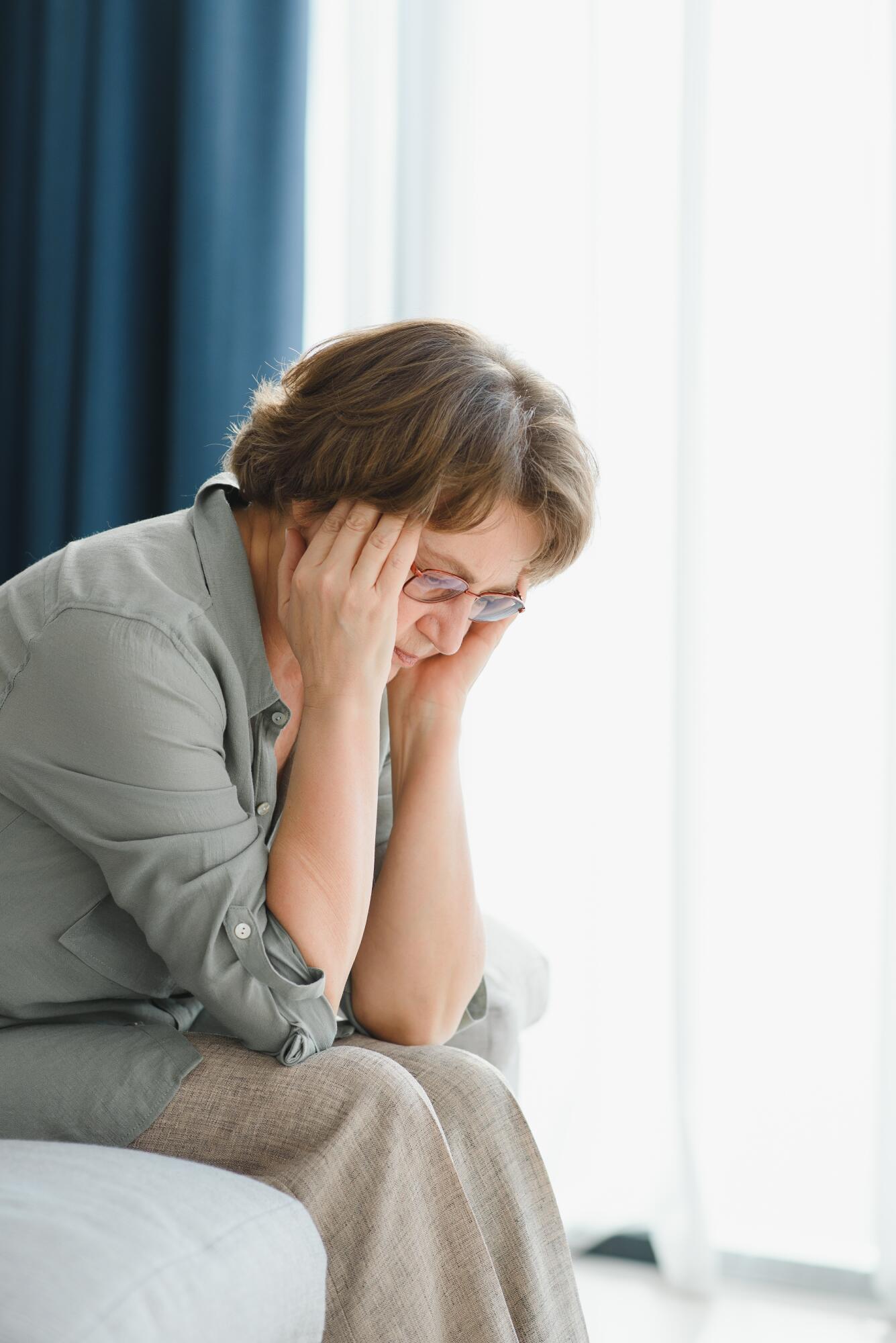 Elderly senior woman massaging her temples to reduce her headache. Older lady feeling scared, anxious, and thinking of sickness or mental health while suffering from a severe migraine or memory loss