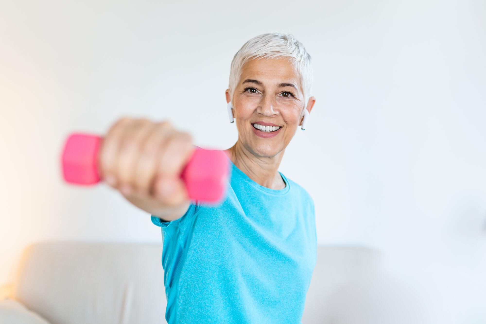 Senior woman exercising with dumbbells at home. Sporty beautiful woman exercising at home to stay fit. Elderly woman exercising at home in a living room. Fitness, workout, healthy living and diet concept.