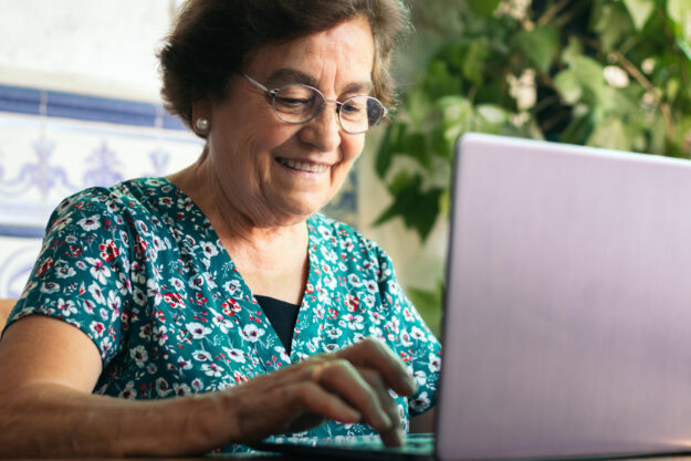 Senior woman with glasses using a laptop and a notebook at home